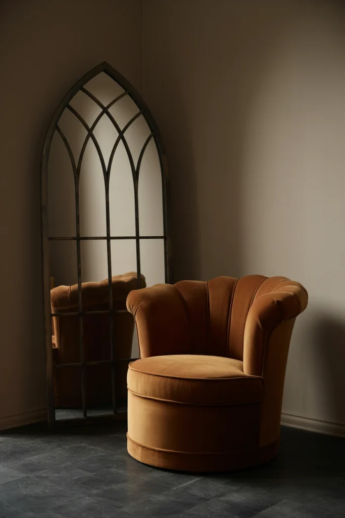 Curved velvet armchair beside a pointed gothic-arch mirror