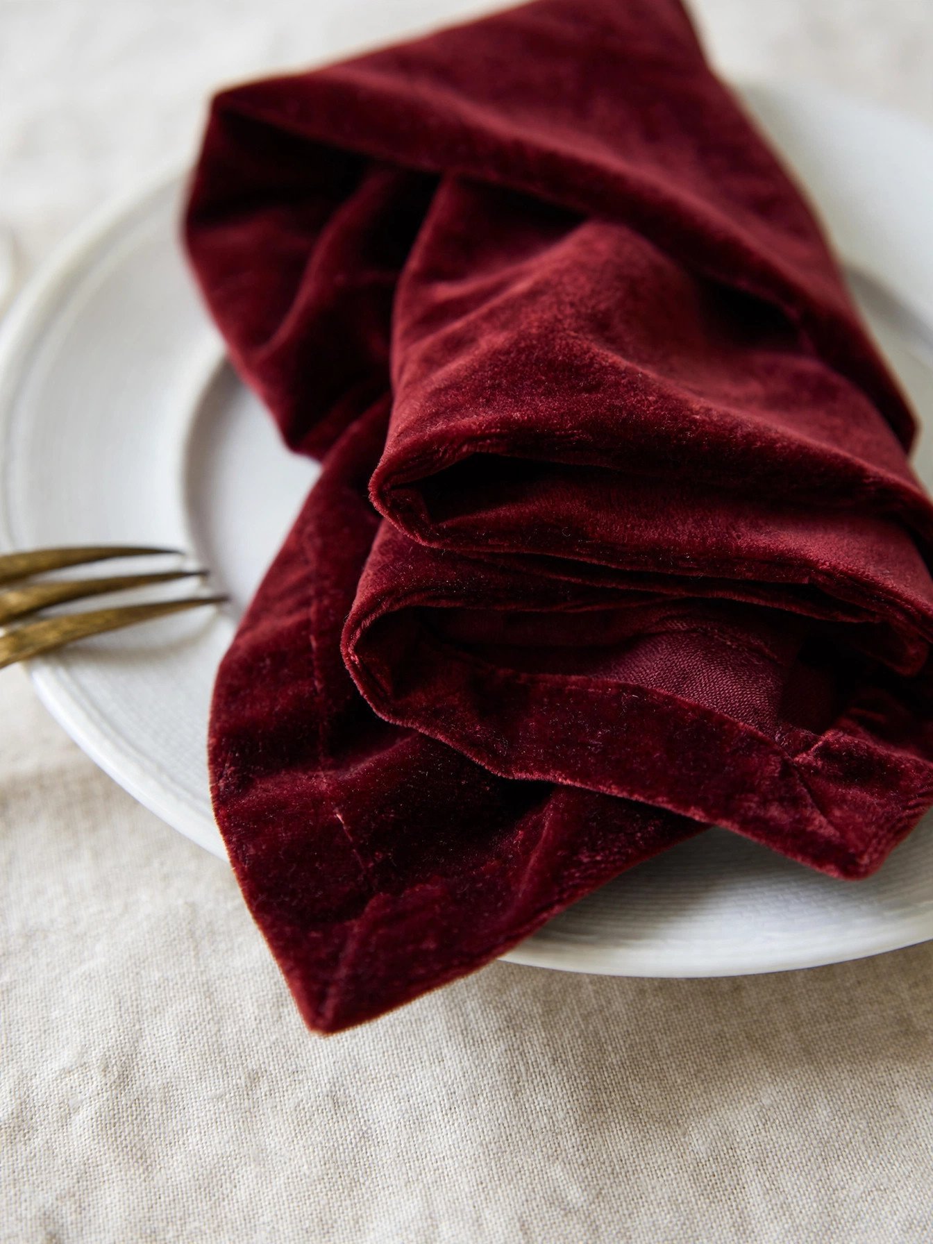 Close-up of a burgundy velvet napkin on a white plate over a pale linen tablecloth
